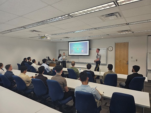 Three presenters in the front of the classroom speaking to a group of adults 