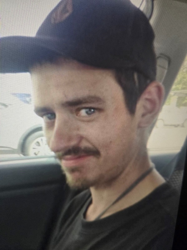 Caucasian male, black baseball hat, blue eyes, black shirt, black mustache.