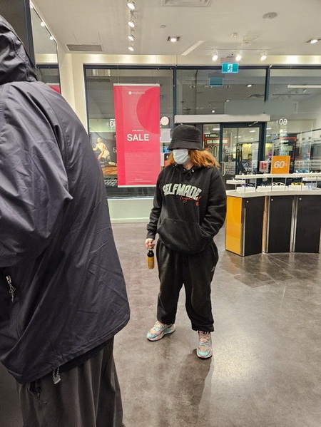 Photo de la femme suspecte portait un masque médical, un chapeau noir, un sweatshirt noir, un pantalon en molleton noir et des chaussures de course blanches à rayures bleues et tenait une bombe aérosol dans sa main droite