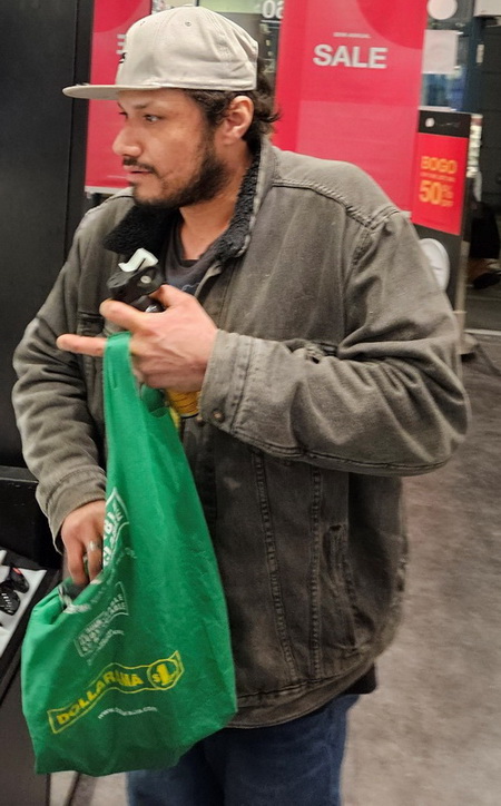 Photo de l’homme suspect portait une casquette de baseball beige, une veste en denim foncé, un chandail noir et un jean bleu, et portait un sac de magasinage vert réutilisable et tenait une bombe aérosol dans sa main