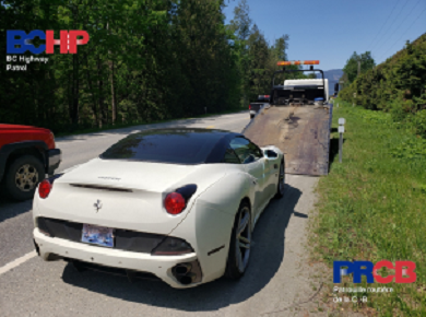 View of white Ferrari car from behind, behind lowered ramp of a flat-deck tow truck.