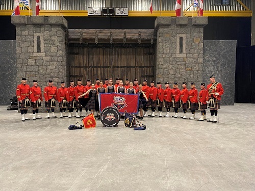 Group photograph of the E-Division Pipes, Drums and Dancers in front of an RCMP 150 banner