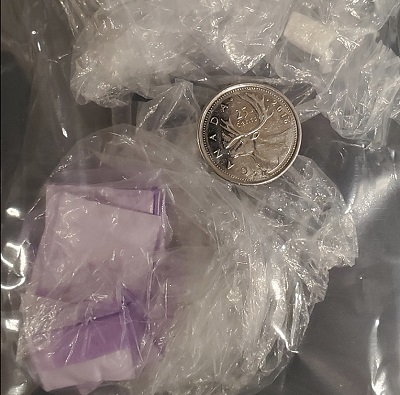 Prepackaged suspected drugs in little purple baggies with a quarter for comparison